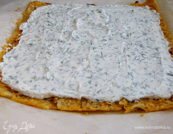 Вынуть готовый морковный корж, перевернуть его на новый лист для выпечки, накрыть мокрым полотенцем и оставить пока не остынет. Затем осторожно снять бумагу и намазать корж приготовленной сырной начинкой.