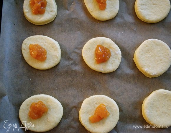 Выложить одну часть кружочков из теста на противень, застеленный пекарской бумагой. Сверху по центу выложить абрикосовый джем...