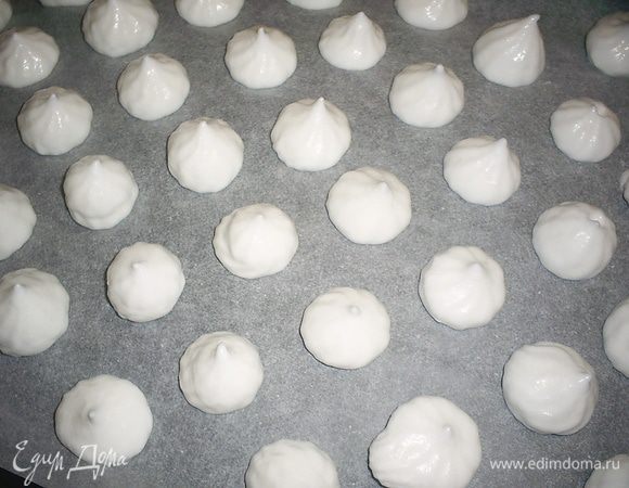 Перекладываем взбитые белки в кондитерский мешок и отсаживаем безешки на противень, выстеленный бумагой для выпечки.  Безе при выпечке не увеличивается в объеме, так что отсаживать их можно довольно плотно. Хочу заметить, что пена настолько нежная, что придать фигурный вид безе вам не удастся. Можете особо и не пытаться. Если мешка кондитерского нет - можете воспользоваться чайной ложкой.