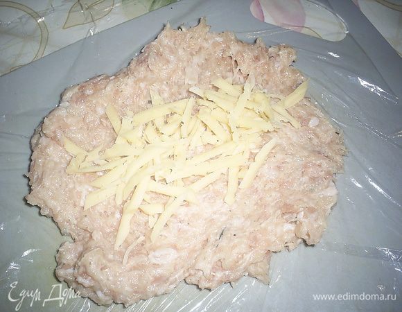 Полученный фарш отбиваем, побросав его немного в миску, и делим на 6 частей. Для формирования сарделек будем использовать пищевую пленку. Одну часть фарша выкладываем на пленку, распределяем по пленке, формируя прямоугольник. Посыпаем заготовку тертым сыром, не доходя до краев. 