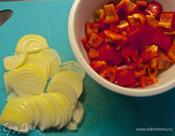 Тем временем лук нарезать полукольцами, а красный сладкий перец кубиками.