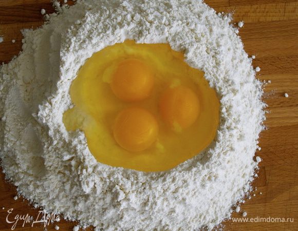 На поверхность стола (или специальной доски для теста) выложить горкой всю муку. Сделать рукой в центре углубление, наподобие лунки. Добавить щепотку соли и разбить в лунку яйца.    