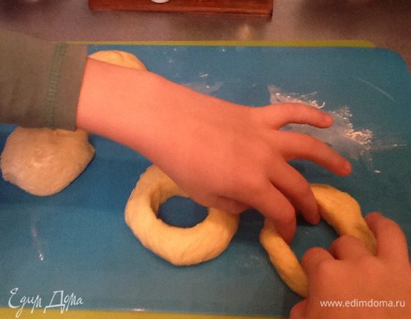 За это время тесто увеличилось в размере  и мы приступаем к самому приятному - формированию бубликов: отделяем маленький кусочек, делаем из него лепешечку и двумя пальцами делаем дырочку в будущем бублике. На фото мне помогает внук, ему очень понравилось  делать дырочки.