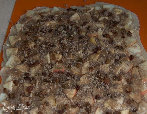 Смазываем 1/3 сливочного масла. Оставляем 1-2 см с одного края, чтобы при скручивание рулет был крепким.
Посыпаем измельченным крекером.
Выкладываем яблоки.
Посыпаем сахаром смешанным с корицей.
Выкладываем изюм.
Посыпаем измельченными орехами.