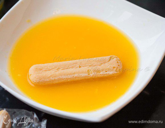 В глубокую и плоскую тарелку выжимаем сок двух апельсинов. Опускаем печенье савоярди в сок на пол минутки.