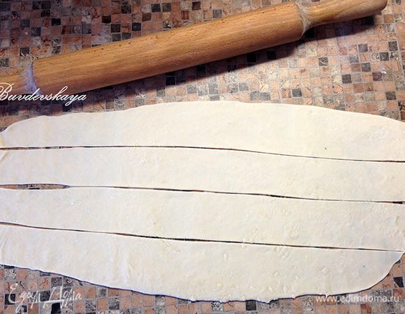 Тесто делим на две части. Одну отправляем обратно в миску и накрываем полотенцем, а вторую часть теста выкладываем на рабочую поверхность, присыпанную мукой. Тесто раскатываем тонко и нарезаем широкими полосками.