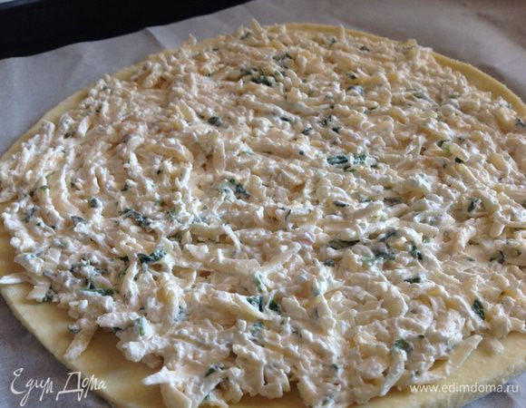 Меньшую лепешку выложить на застеленный пергаментной бумагой противень и распределить сырную начинку по всей площади.