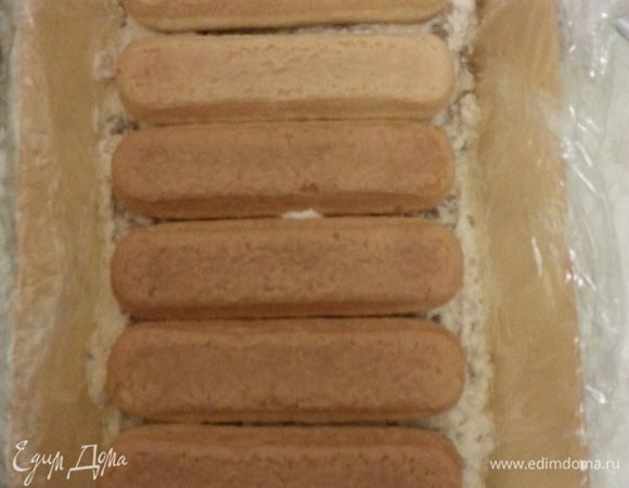 В форму застеленную пищевой пленкой выкладываем часть крема, сверху - печенье, которое предварительно макаем в молоко.