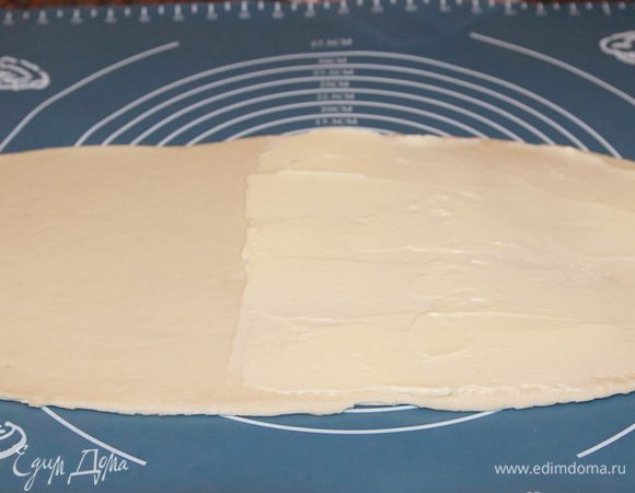 Когда тесто поднялось, хорошо обминаем, затягиваем миску вновь пленкой и убираем в холодильник на 1 час. Тесто вновь удвоится в размере. Вновь обминаем его и убираем в морозильную камеру на 30 минут. 75 г сливочного масла (масло необходимо сильно размягченное, но не талое) разминаем шпателем или вилкой. Достаем тесто и раскатываем его в прямоугольный пласт, чтобы длина была как минимум в три раза больше, чем ширина. При этом получится толщина около 4 мм. Масло делим пополам и наносим ровным слоем одну половину на половину пласта теста. Даем полежать 10 минут.