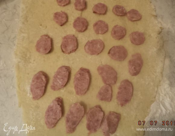 Колбасу нарезать тонкими ломтиками. Выложить ломтики на пласт теста довольно близко друг к другу, края необходимо оставить без начинки.