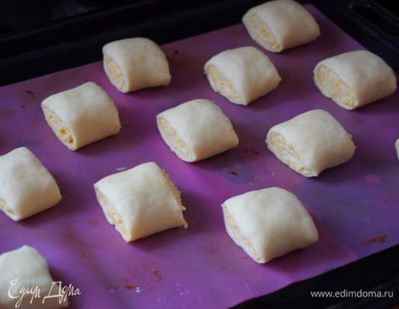 Порезать рулетик, выложить на противень, смазать яйцом, включить духовку разогреваться.