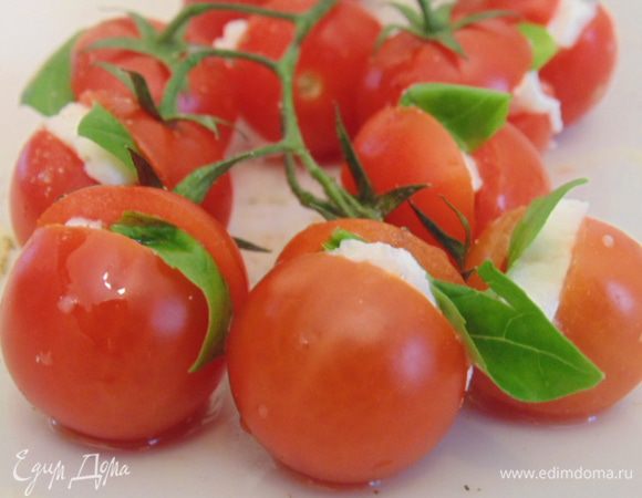 На помидорках сделать надрезы, вставить кусочек моцареллы и листик базилика. Сбрызнуть отливковым маслом, посолить и поперчить.