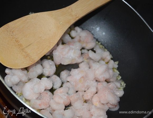 Тем временем, поставьте на огонь глубокую сковороду, налейте в нее оливковое масло и выдавите чеснок, в течение нескольких секунд разогрейте, затем добавьте креветки и оставьте на среднем огне. Мелко нарубите петрушку и отложите пока ее в сторону.