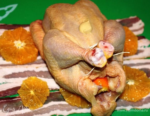 Бекон разложить полоска к полоске, на него выложить апельсин. Ножки цыпленка связать, тушку смазать горчицей (острой), внутрь уложить корки от апельсина и расположить цыпленка на беконе.