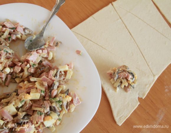 На каждый треугольник теста выложить по столовой ложке начинки, завернуть в виде рогалика, начиная с широкого края.