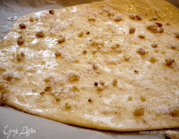 Растапливаем масло. Духовку разогреваем до 180 градусов. Противень накрываем пергаментом. Тесто выкладываем на присыпанную мукой поверхность и сформировав из него батон, делим его на шесть равных частей. Присыпаем поверхность и первую часть теста мукой и раскатываем тесто в прямоугольный пласт как можно тоньше, примерно до 1 мм. Выкладываем на пергамент. Смазываем растопленным маслом, присыпаем  1/6 частью начинки. 