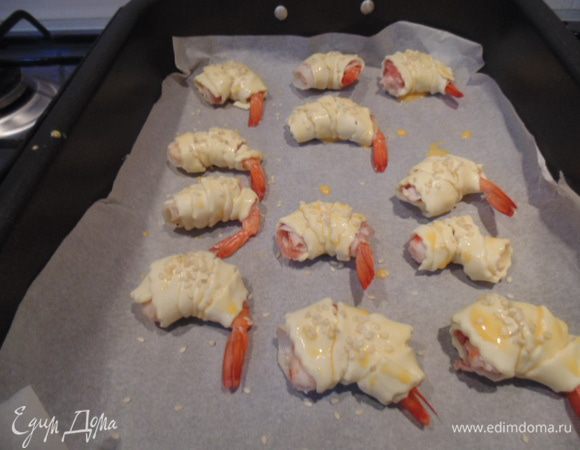 Тесто нарезать тонкими полосками, обернуть каждую креветку полоской теста. Желток взбить, добавить молоко. Каждую креветку смазать желтком, посыпать кунжутом. Запекать при температуре 200 гр С 15-20 минут до зарумянивания.