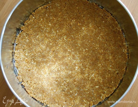В разъемную форму (24 см) выложить мокрую крошку печенья и разровнять по дну формы. Убрать в холодильник на полчаса. 