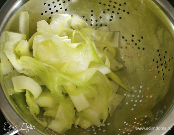 Цукини очистить от кожицы. С помощью овощечистки нарезать кабачок тонкими полосками-лентами. Положить в дуршлаг, посолить, перемешать и дать постоять около 10 минут. 