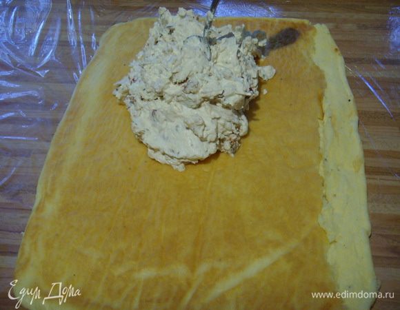 Тесто вынуть из духовки вместе с пергаментом и перекинуть на подготовленную заранее пищевую плёнку в размере большем, чем поверхность теста. 