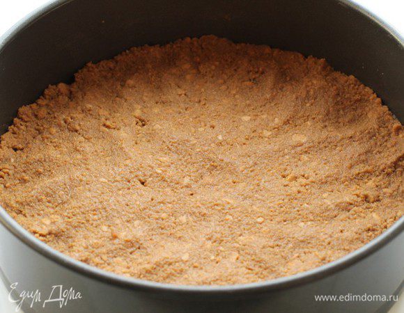 Соединить крошку с размягченным сливочным маслом, хорошо перемешать и выложить в застеленную пергаментом форму. Утрамбовать. Убрать в холодильник до тех пор, пока будет готовиться начинка.