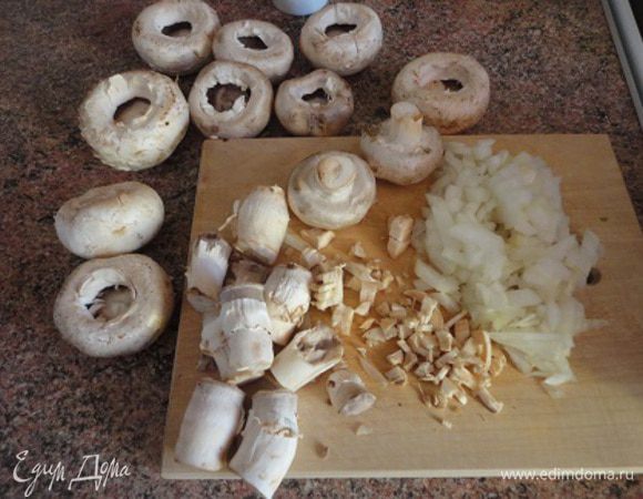 У шампиньонов открутить ножки, немного обрезать края и ложечкой выбрать перегородки. Все мелко порубить. Луковицу нарезать мелкими кубиками. В сковороде разогреть растительное масло, обжарить на нем вначале лук до прозрачности, добавить грибы, потушить пару минут.