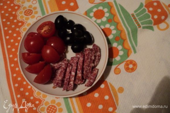 Колбасу нарезать тонкими ломтиками, затем кусочками, помидорчики черри, нарезать напополам, нарезать оливки.