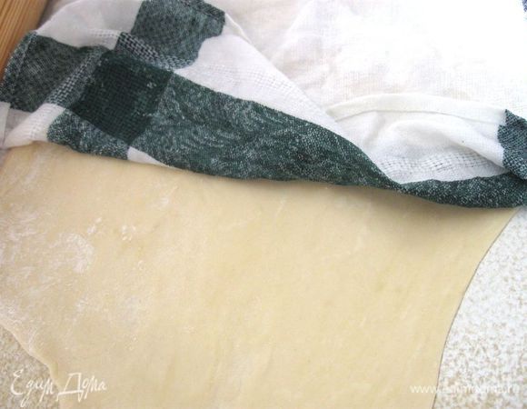 Разделить на 2 куска, сделать из них лепешечки руками. Аккуратно растянуть каждую во все стороны на столе или доске, чуть присыпанной мукой. Немного раскатать скалкой. Оставить тесто под влажным полотенцем минут на 5. 
