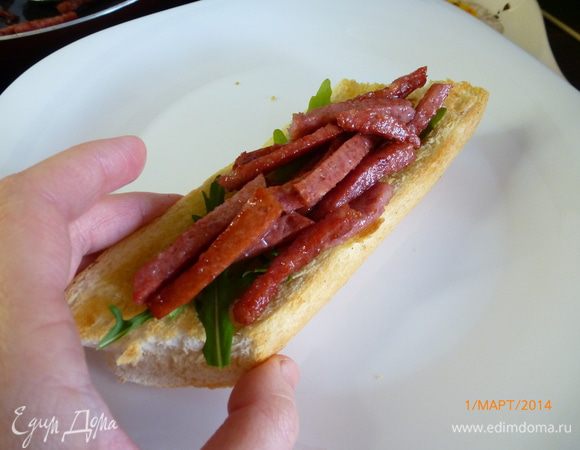 На кусочки багета выкладываем немного руколы, далее колбаса, обильно поливаем соусом, опять рукола и закрываем вторым куском багета.