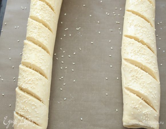 Выложить  рулеты на бумагу для выпечки. Смазать взбитым яйцом или молоком. Посыпать кунжутом и сделать косые надрезы. 