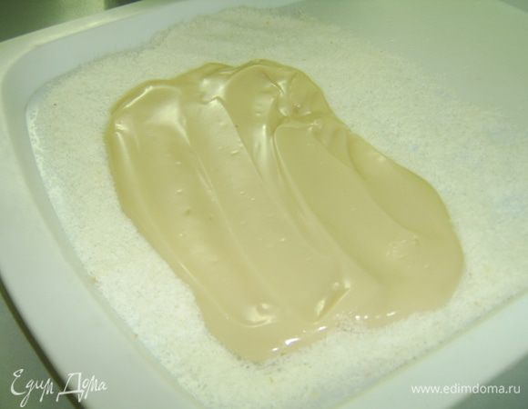 На противень расстелить целлофан и щедро посыпать кокосовой стружкой. Дать смеси немного остыть и выложить на противень,  разровнять в слой толщиной 1 см.