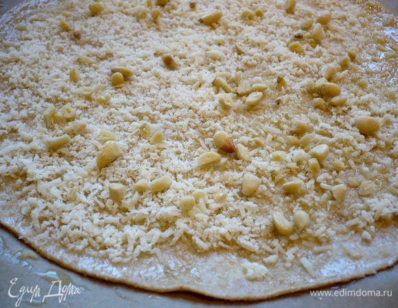 Тесто делим на шесть частей. Духовку разогреваем до 250 градусов. На присыпанной мукой поверхности раскатываем первую часть теста в тоненькую лепешку, затем подравниваем края, положив сверху дно от формы (у меня диаметром 24 см). Можно затем использовать форму для выпечки и собирать пирог в ней, а можно, как я, сделать пирог куполом и тогда выкладывать слои теста и начинку прямо на постеленную на противень пекарскую бумагу. Первый слой смазываем оливковым маслом. Посыпаем 1/6 частью  пармезана и 1/5 частью порубленных орешков. 