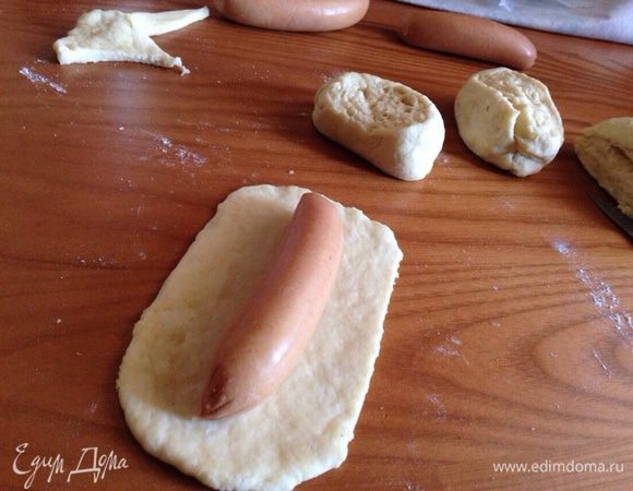 Разделить тесто на 10-12 частей. Одну из них оставить для формовки лапок и ушек. Раскатать одну часть, сверху на тесто положить сосиску.