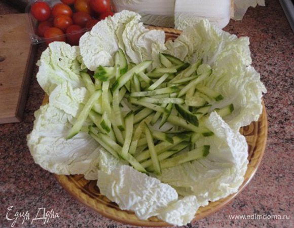 Листья капусты выложить на блюдо. Огурцы нарезать соломкой и выложить сверху.