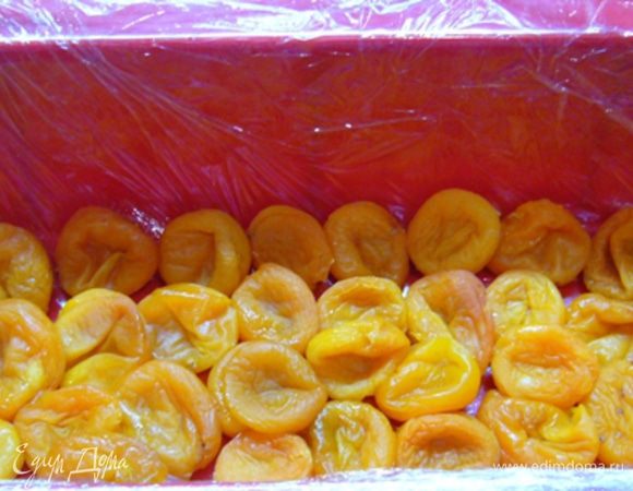 Переходим к сборке. Форму застелить пищевой пленкой.
На дно уложить целую курагу.