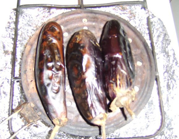 Для начала нужно запечь баклажаны на гриле, я даже придумала один глагол для этого - "закебабить". Выбирайте плотные, небольшие, неизогнутые (прямы!) баклажаны с плодоножками. Затем надо сделать несколько надрезов (или проколов) на кожице. Запекать лучше на огне, но не у каждого ведь есть возможность поставить мангал, поэтому мне больше нравится запекать на газовой плите на рассекателе (перед этим лучше застелить плиту алюминиевой фольгой, дабы потом не истязать себя ее очищением :)). Можно и в духовке, но в оригинале это открытый огонь. Не срезайте с баклажанов плодоножку, она пригодиться для переворачивания! "кебабить" надо до черноты, тогда кожица будет очень легко отходить. Итак, баклажаны (у меня 8 небольших) запекли, охладили, сняли кожицу, и мелко порезали. Сложили все в кастрюлю и поставили на небольшой огонь.