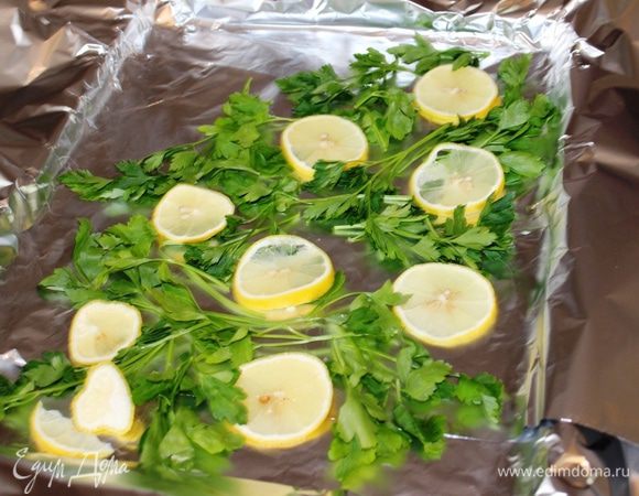 На противень выстелить фольгу в несколько слоев, разложить кружочки лимона и веточки свежей петрушки (по диагонали).