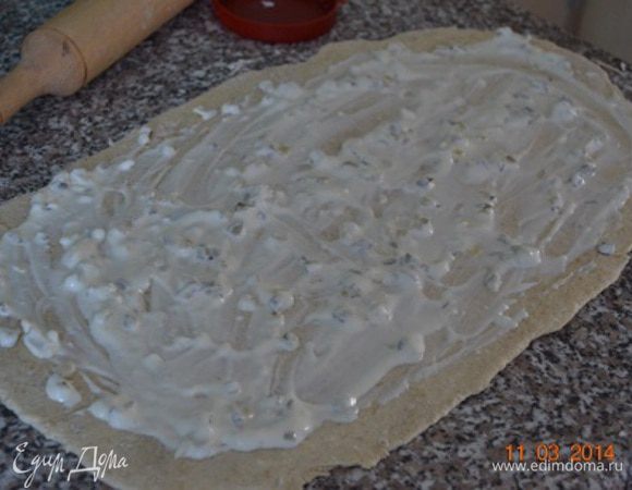 Отдохнувшее тесто раскатать в тонкий прямоугольный пласт и смазать майонезом с чесноком