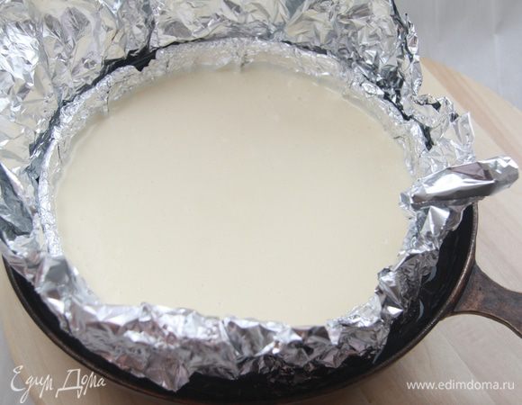 Вылить сырную смесь на корж. Теперь соорудить такую конструкцию: обернуть форму двумя слоями фольги, поместить в ёмкость (у меня это старая чугунная сковорода), наполненную до 2/3 высоты формы водой.