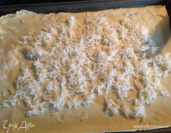 Раскатать тесто на противне и равномерно выложить на него отварной рис. 