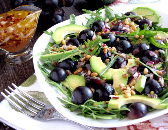 Авокадо очистить, нарезать ломтиками, сбрызнуть лимонным соком и выложить на рукколу. Виноград разрезать пополам, разбросать сверху авокадо. Полить заправкой. Посыпать кедровыми орешками.