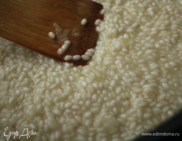 После того, как вино полностью впитается в рис, небольшими порциями влить куриный бульон. Рис нужно непрерывно перемешивать лопаткой.