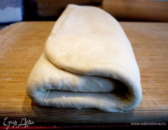 Снова достаем тесто, раскатываем его на присыпанной мукой повехности. Сворачиваем его дважды. 