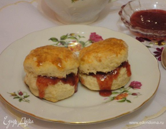 На присыпанной мукой поверхности раскатать лепешку толщиной в 2 - 2,5 см и вырезать кружки диаметром 5 см. Вырезать не прокручивая . Для этого форму для вырезки ( у меня рюмка) периодически обмакивать в муке. 
Выложить на лист. При желании можно смазать сверху яичным желтком и выпекать 12-15 минут. Подавать к чаю с клубничным джемом, вареньем, жирной сметаной с творогом или взбитыми сливками.
