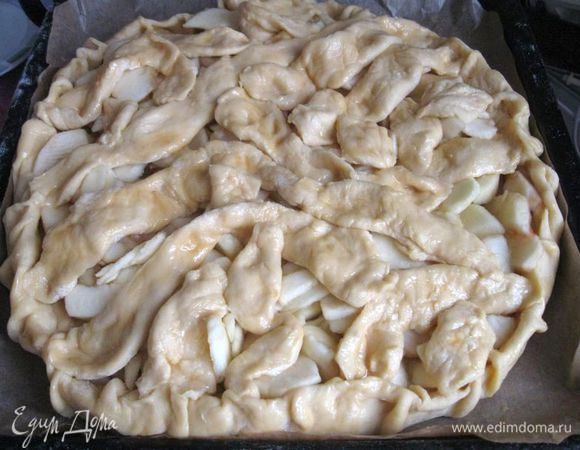 Положить на застеленный бумагой для выпечки противень нижнюю часть теста. Сверху положить начинку. Из «колбасок», раскатав их,  сделать плоские листочки, полоски, смазать их кисточкой яйцами, смешанными с содой, и положить на начинку в произвольной форме.