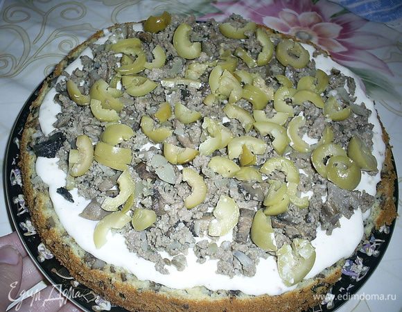 Теперь кладем на блюдо один бисквитный корж срезом вверх. Смазываем третей частью крема. Равномерно распределяем мясную прослойку, посыпаем мелко нарезанными оливками.