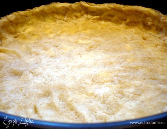 Дно у формы диаметром 26 см выложим пекарской бумагой.  Тесто присыпем мукой и раскатаем на присыпанной мукой поверхности. Выложим тесто в форму, образуя бортики. 