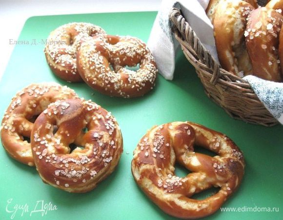 Растворить пищевую соду в 1 литре воды и довести воду с содой до кипения. Убавить огонь, вода должна чуть – чуть кипеть во время  всего процесса.  Шумовкой опускать по одному каждый брецель  в воду на 15-20 секунд (они увеличатся немного в размере), затем вынуть и вернуть его на противень, застеленный пекарской бумагой.  Каждый брецель  после того, как он вынут из воды, тут же присыпать морской солью или кунжутом. Можно сделать острым  ножом с тонким лезвием  горизонтальный неглубокий надрез на средней утолщенной части, как бы «запрограммировать»  трещинку в  выпечке.  Разогреть  духовку до 220 градусов. 