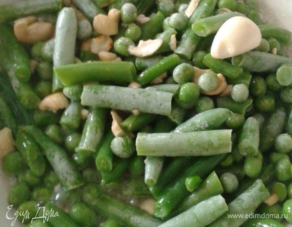 На сухой сковородке слегка поджарьте орешки кешью. Добавьте растительное масло, чеснок затем выложите стручковую фасоль и зеленый горошек и быстро обжарьте 3-5 минут.
