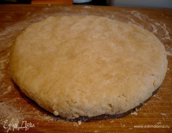 Разделим тесто на две части. Выложим первую часть на хорошо присыпанную мукой поверхность, сформируем лепешку и выльем на нее ложечку растительного масла, сформируем шар и снова — лепешку. Присыпем ее сверху мукой и раскатаем в круг толщиной примерно 0,5 см. 